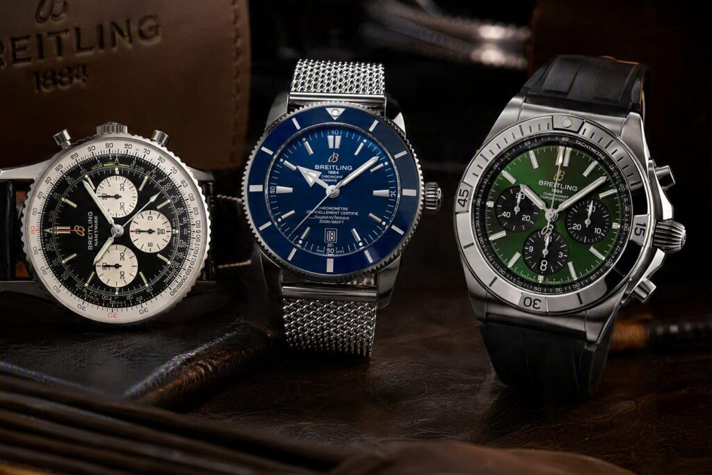Drei Breitling-Chronographen nebeneinander vor einem Lederetui: Navitimer, Superocean Heritage mit blauem Zifferblatt und Chronomat mit grünem Zifferblatt